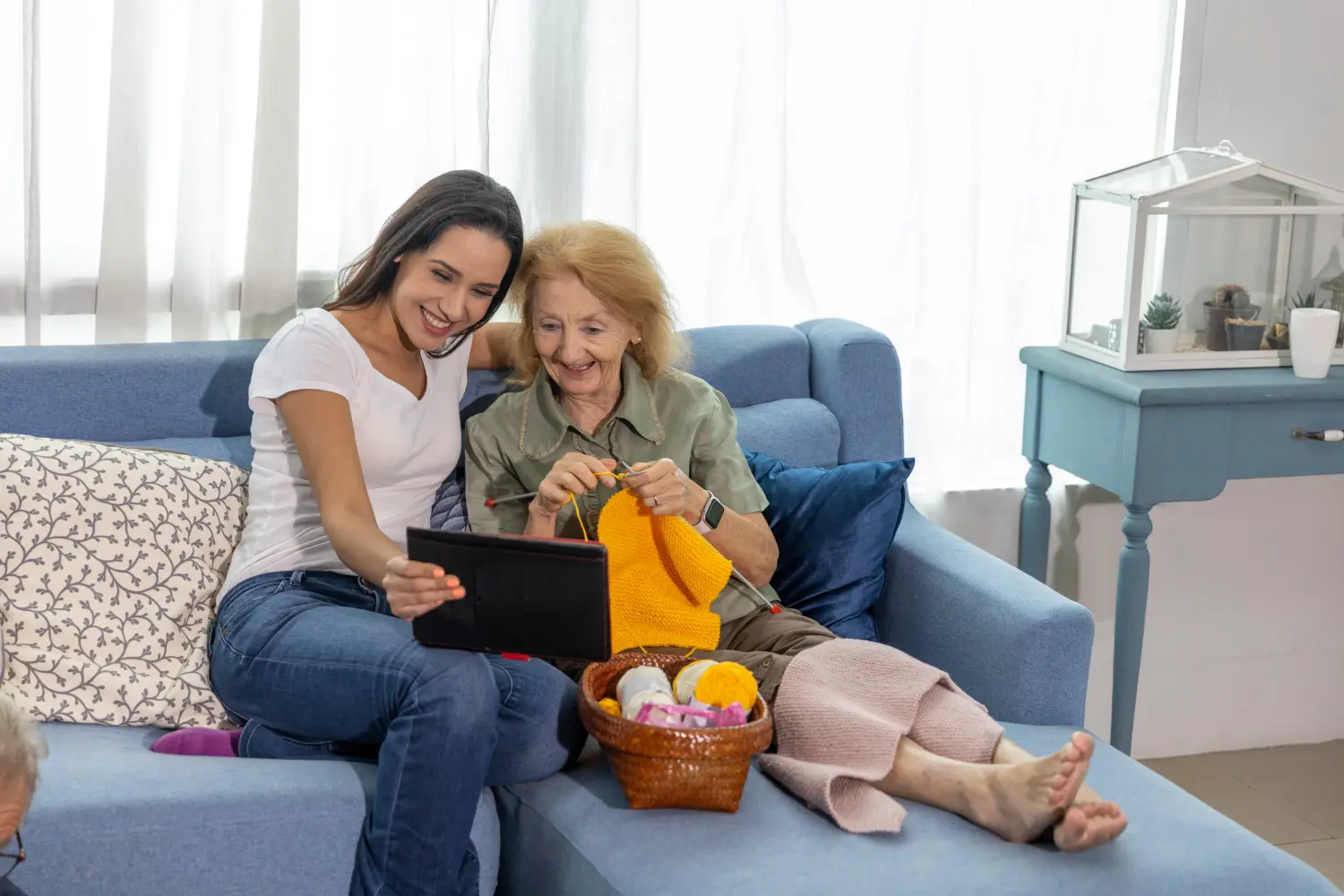 Moment des Familienglücks zwischen einer Krankenschwester und einer alten Dame in einem Haus, die strickt und online Muster überprüft.